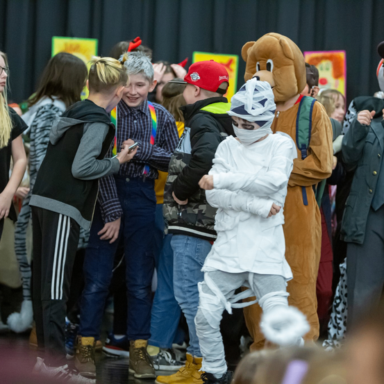 Eine Gruppe von Menschen bei einer Schulveranstaltung, die Kostüme tragen. Eine Person trägt ein Mumienkostüm und hält ein Handy.