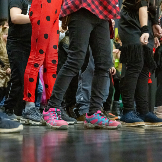 Mehrere Menschen stehen in einer Reihe, einige tragen Turnschuhe, andere Stiefel. Eine Person trägt rote Leggings mit Punkten.