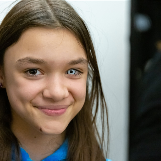 Ein lächelndes Mädchen mit braunen Haaren und blauen Augen in einem blauen Shirt posiert für ein Foto.