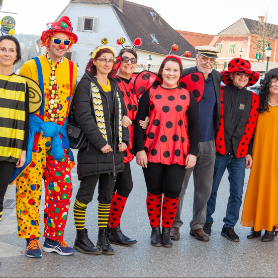 Eine Gruppe von Menschen in Clown- und Marienkäferkostümen steht in einer Reihe auf einer Straße.