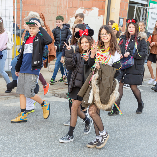 Eine Gruppe junger Leute geht eine Stadtstraße entlang, einige tragen Mickey-Mouse-Ohren und halten Friedenszeichen. Eine hat einen Rucksack.
