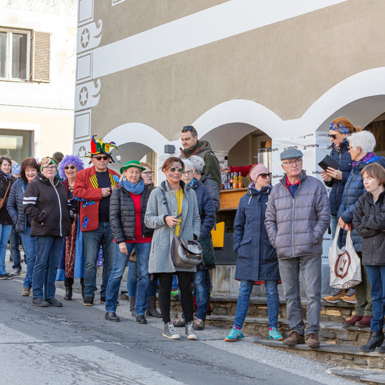 Eine Gruppe von Menschen in verschiedenen Kostümen und mit Sonnenbrillen steht auf den Stufen eines Gebäudes, während andere auf der Straße gehen.