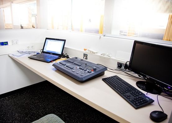 Ein Büroschreibtisch ist mit einem Laptop, einem Monitor, einer Tastatur, einer Maus und einem Lichtsteuerungspanel ausgestattet.