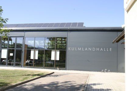Ein modernes Gebäude mit Glasfenstern und Solarmodulen auf dem Dach, gekennzeichnet mit Kulmlandhalle.