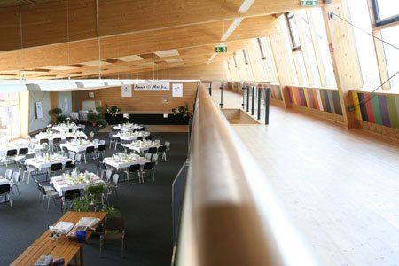 Ein Indoor-Veranstaltungsraum mit Holzwänden, einer Galerie und mehreren Tischen, die für eine Zusammenkunft vorbereitet sind.