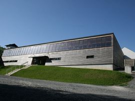 Ein großes modernes Gebäude mit Solarpaneelen auf dem Dach, umgeben von einem grünen Rasen und einer Auffahrt.