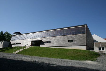 Ein modernes Gebäude mit großen Glasfenstern und einem Grashang unter einem klaren blauen Himmel.