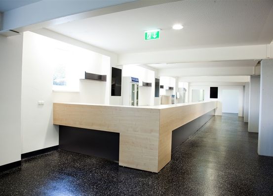 Ein leeres Büro mit einer hölzernen Theke, weißen Wänden, schwarzen Böden und einer Decke mit einem Notfallausgangsschild.