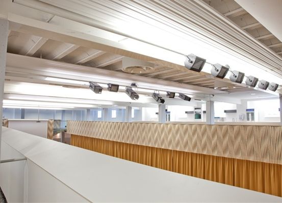 Ein Büroraum mit weißer Decke und beige gemusterter Wand, beleuchtet von linearen Leuchtstoffröhren.