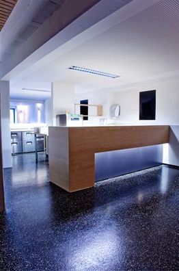 Ein Innenraum mit einem hölzernen Empfangstresen, schwarzem gesprenkeltem Boden und einer weißen Wand mit einem montierten Bilderrahmen.