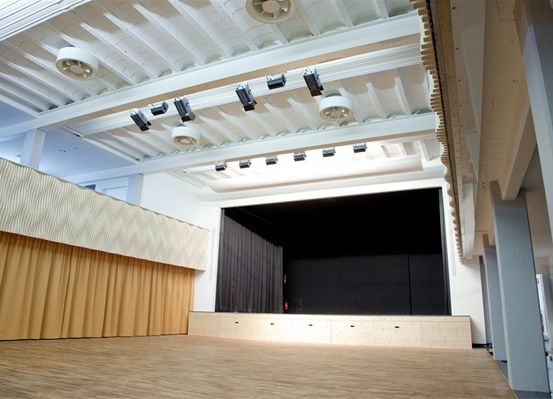 Eine leere Bühne mit schwarzem Vorhang, Holzboden und einer Decke mit Lichtern.