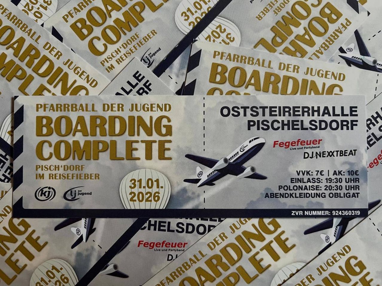 Ein Nahaufnahme von Boarding Complete Eventkarten, mit einem Flugzeug, goldenem Text und einem Bild eines Ballons. Der Text beinhaltet das Datum '31.01.2026', den Veranstaltungsnamen 'Fegefeuer' und 'Oststeiererhald Pischelsdorf'.