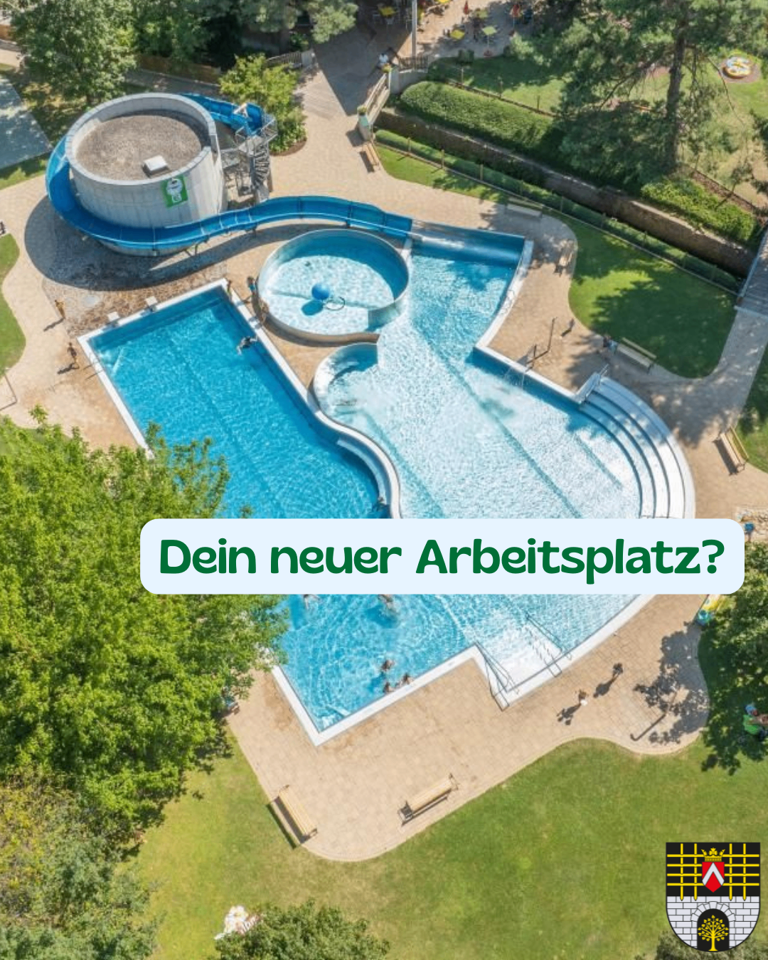 Aerial view of a large swimming pool with a water slide and people swimming. The pool is surrounded by green grass and trees. The image has a watermark with the text 'Dein neuer Arbeitsplatz?'.