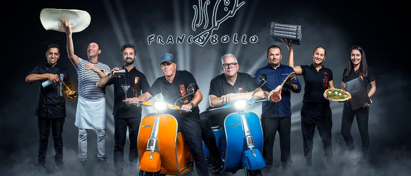 Eine Gruppe von Menschen steht mit Rollern, zwei sitzen auf blauen und orangefarbenen Rollern, halten eine Pizzaschachtel und einen Teller mit Essen, tragen Uniformen und Mützen, mit einem Logo an der Wand.