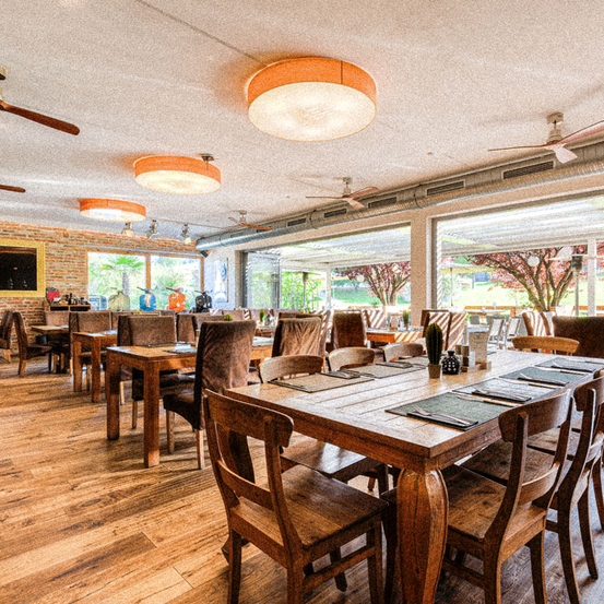 Ein Restaurant mit Holzböden und -wänden. Es gibt mehrere Holztische und -stühle. Jeder Tisch hat einen Kaktus und eine Tischdecke.