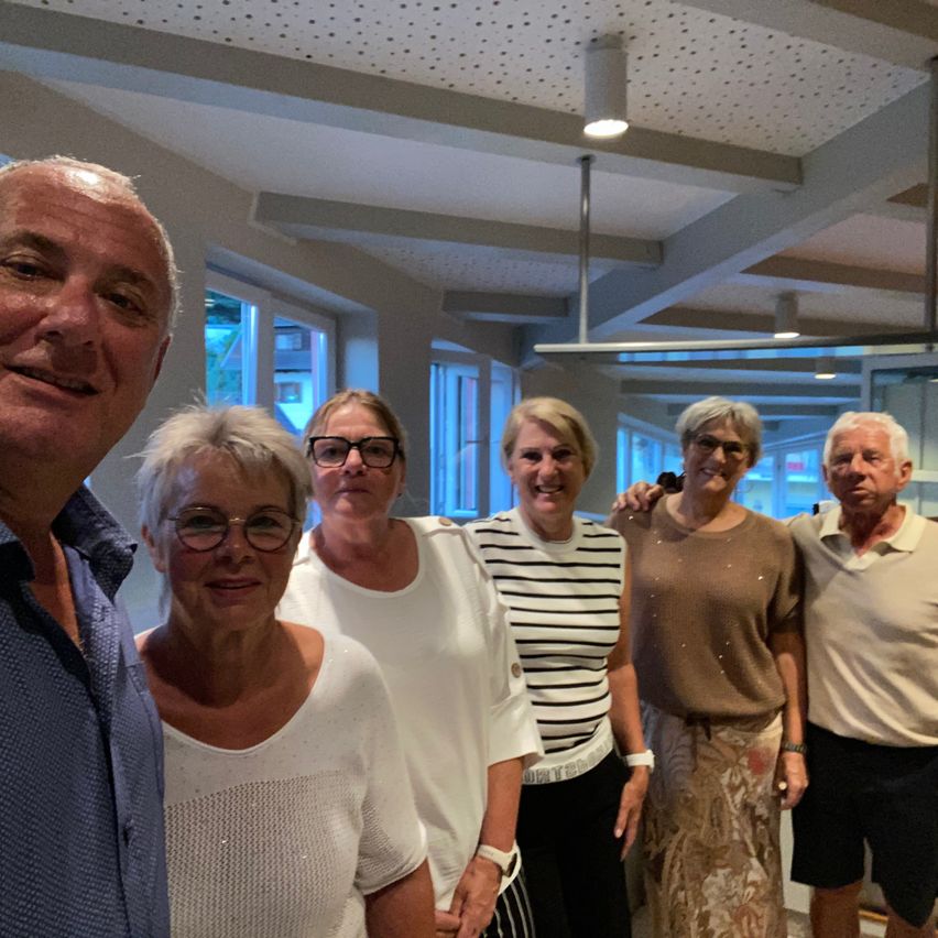Eine Gruppe von fünf Personen, darunter ein Mann und vier Frauen, stehen zusammen in einem Raum und lächeln für ein Foto.