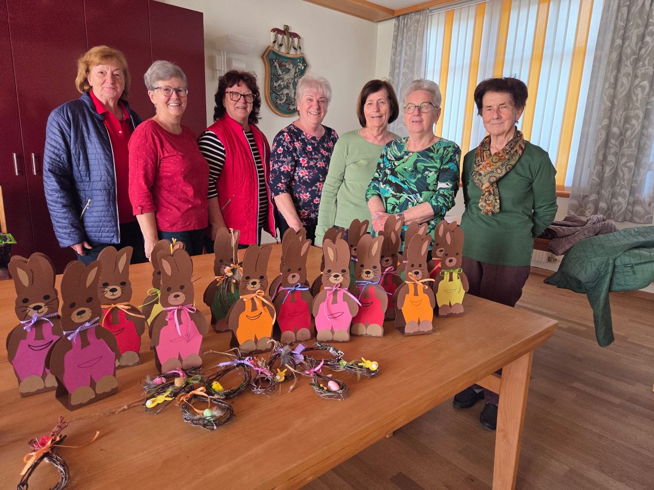 Eine Gruppe von Frauen steht hinter einem Tisch mit selbstgemachten Osterhasen und Dekorationen. Sie lächeln und scheinen für ein Foto zu posieren.
