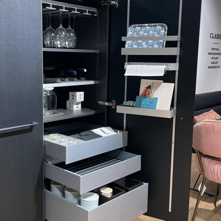 Eine moderne Küchenvorratskammer mit mehreren Regalen und Schubladen, die Weingläser, Flaschen und Küchenutensilien enthält. Die Vorratskammer hat ein elegantes schwarzes und weißes Design.