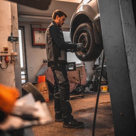 Ein Mann in einer Garage, der an einem Autoreifen arbeitet und ein Werkzeug hält.