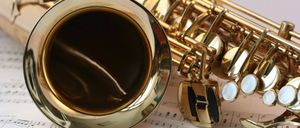 Eine Nahaufnahme eines glänzenden Messingsaxophons auf einem offenen Musikbuch mit Musiknoten.