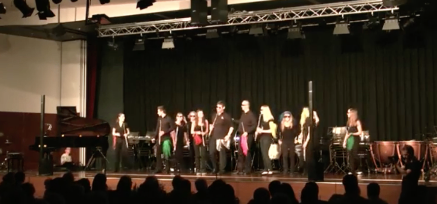 Eine Gruppe von Musikern tritt auf einer Bühne mit Klavier, Schlagzeug und anderen Instrumenten vor einem Publikum auf.