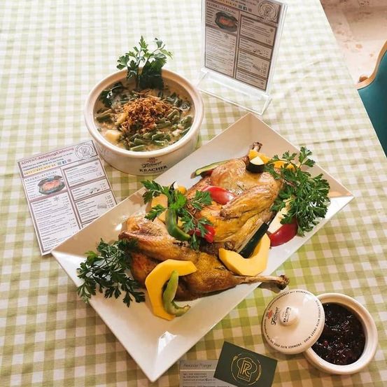 Ein Tisch mit einem weißen Teller mit gebratenem Huhn, geschmückt mit Gemüse, einer Schüssel grüner Bohnensuppe und einer Menükarte.