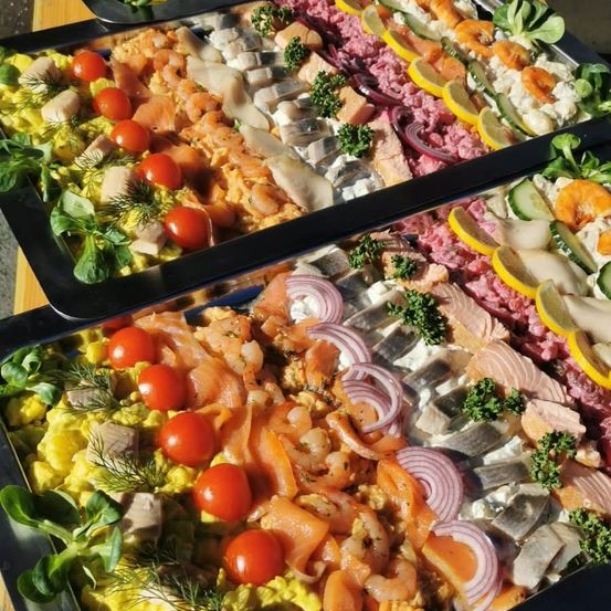 Ein Buffettisch mit verschiedenen Meeresfrüchten, einschließlich Lachs, Garnelen und Fischscheiben, garniert mit Zitronen, Tomaten und Kräutern.