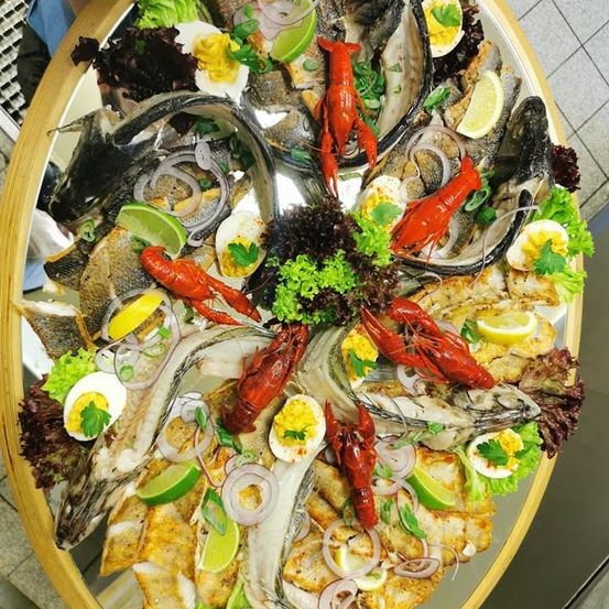 Ein großer Teller mit Meeresfrüchten, einschließlich Fisch, Hummer und Garnelen, garniert mit Zitronenscheiben, Frühlingszwiebeln und Petersilie, in einem kreisförmigen Muster angeordnet.