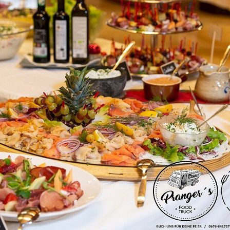 Ein Buffettisch mit einer großen Platte mit Lachs, Trauben und verschiedenen Gemüsesorten, begleitet von Dips, Oliven und einer Ananas als Mittelpunkt.