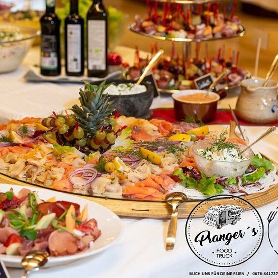 Ein Buffettisch mit einer großen Platte mit Lachs, Trauben und verschiedenen Gemüsesorten, begleitet von Dips, Oliven und einer Ananas als Mittelpunkt.