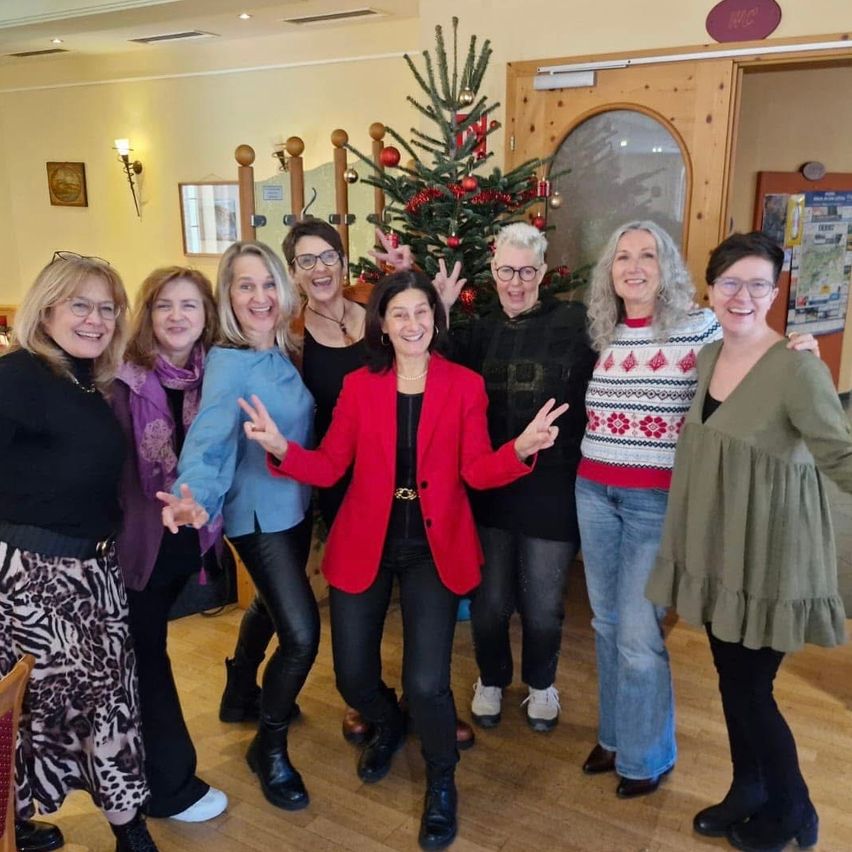 Eine Gruppe von Frauen in Winterkleidung posiert für ein Foto vor einem geschmückten Weihnachtsbaum in einem Raum.