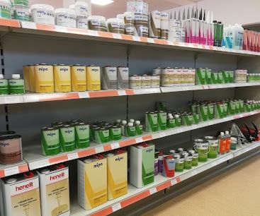 Ein Ladenregal mit verschiedenen Farben- und Lackdosen, in Reihen angeordnet, wobei grüne und gelbe Behälter hervorgehoben sind. Die Regale haben orangefarbene Ränder.