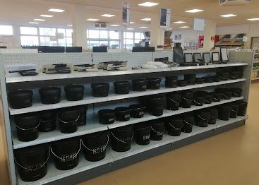 Ein Laden mit mehreren Regalen, die mit schwarzen Eimern gefüllt sind. Jeder Eimer hat ein weißes Etikett mit Text darauf, und es gibt zusätzliche Artikel auf den Regalen.