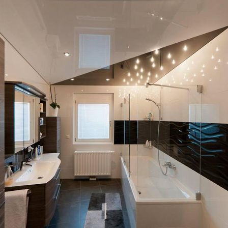 Ein modernes Badezimmer mit einer weißen Badewanne, einer Glasdusche und schwarz-weißen gefliesten Wänden. Ein Waschbecken mit einem Wasserhahn und einem Spiegel befindet sich links, und ein Heizkörper ist an der Wand angebracht.
