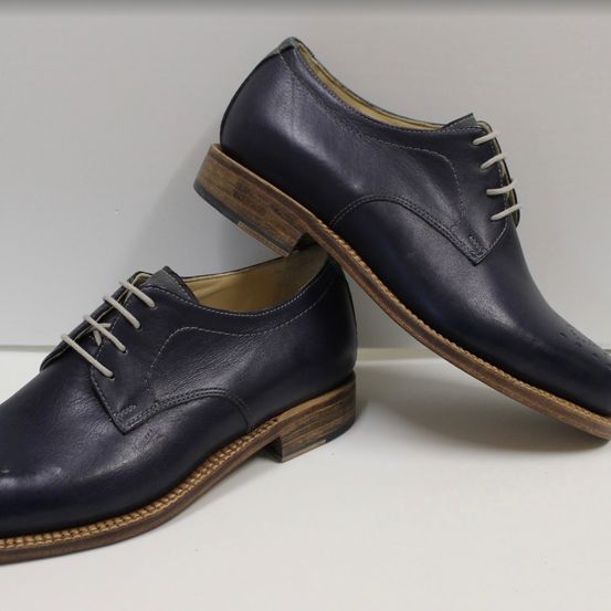 Ein Paar marineblaue Lederschuhe mit braunen Sohlen und weißen Schnürsenkeln, auf einem weißen Hintergrund präsentiert.