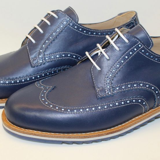 Ein Paar dunkelblaue Lederschuhe mit dekorativen Nieten und weißen Schnürsenkeln. Die Schuhe haben braune Sohlen und sind auf einer weißen Oberfläche ausgestellt.