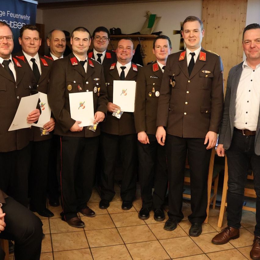 Eine Gruppe von Männern in Militäruniformen steht zusammen, hält Urkunden und posiert für ein Foto. Hinter ihnen zeigt ein Banner ein Logo.