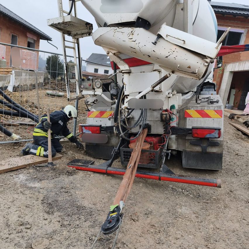 Ein Bauarbeiter kniet und hält ein Werkzeug in der Nähe eines großen Zementmischers auf einer Baustelle.