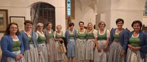 Eine Gruppe von Frauen in traditioneller bayerischer Kleidung steht in einer Kirche. Sie lächeln für die Kamera.