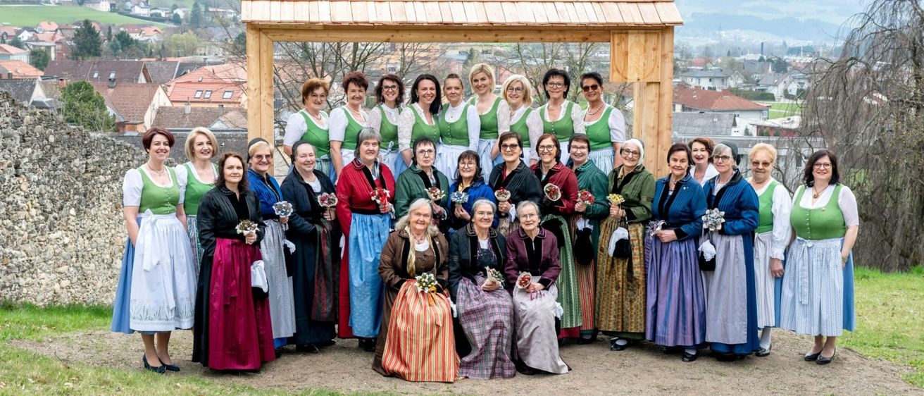 Eine Gruppe von Frauen in traditioneller Kleidung posiert für ein Foto in einer malerischen Gegend mit Bergen im Hintergrund.
