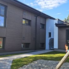 Das Äußere eines Gebäudekomplexes mit braunen Holzverkleidungen, mit mehreren Fenstern und einem Weg, der zu einer Treppe führt.