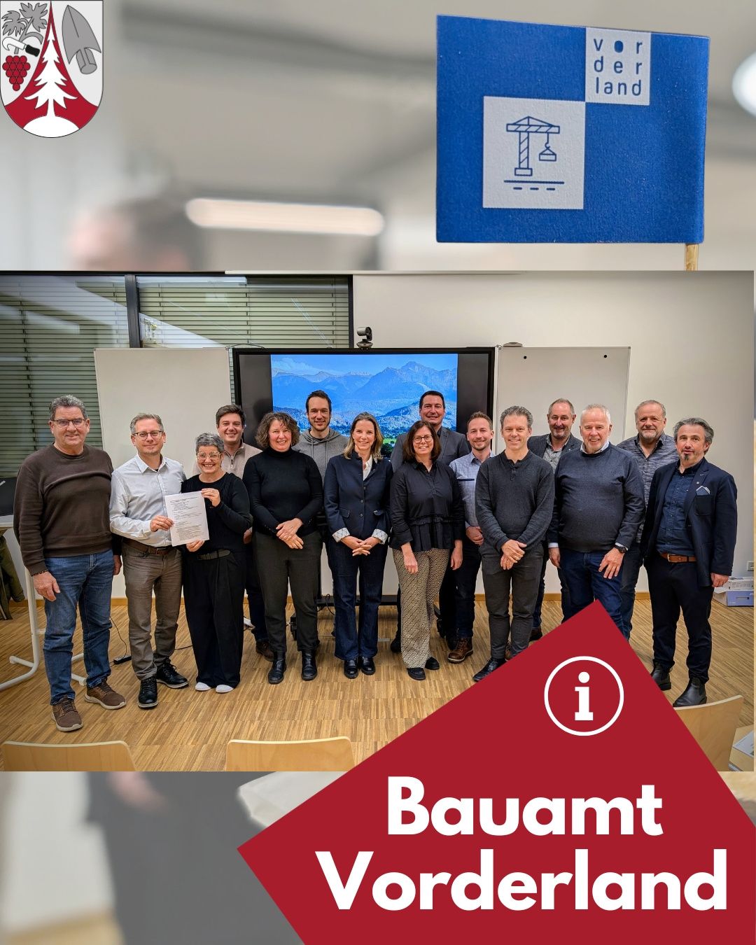 Eine Gruppe von Menschen posiert für ein Foto in einem Besprechungsraum. Ein Mann in der Mitte hält ein Zertifikat. Hinter ihnen befindet sich eine Tafel und ein Fernseher an der Wand.