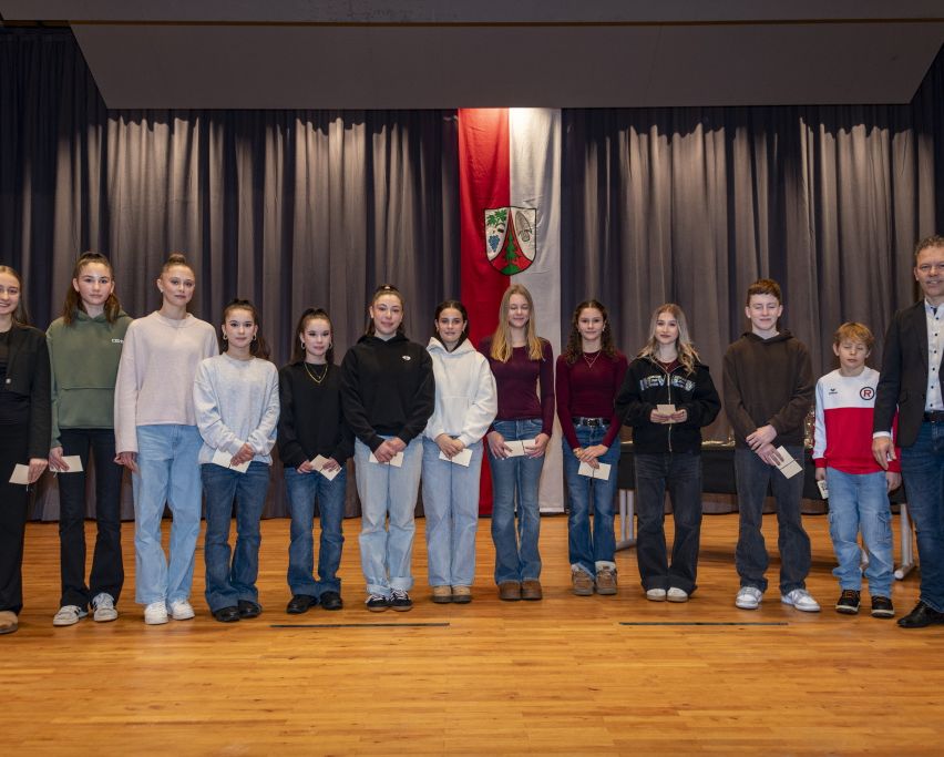 Gruppe junger Menschen in Freizeitkleidung mit Urkunden auf der Bühne.