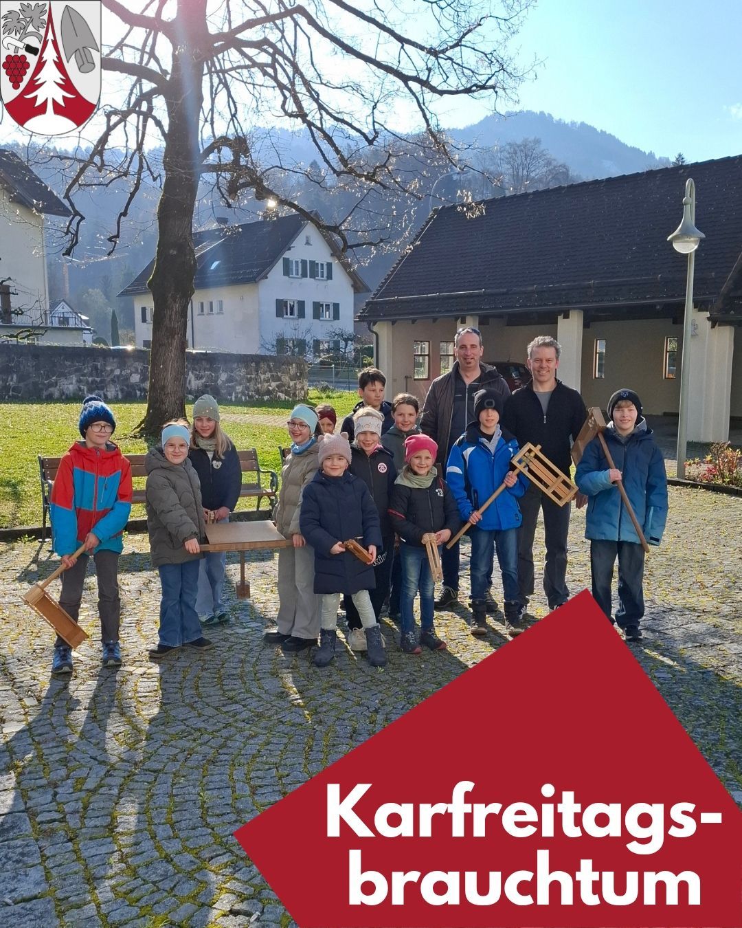 A group of children and two adults holding wooden sleds stand outside in a village, with houses and a tree in the background.
