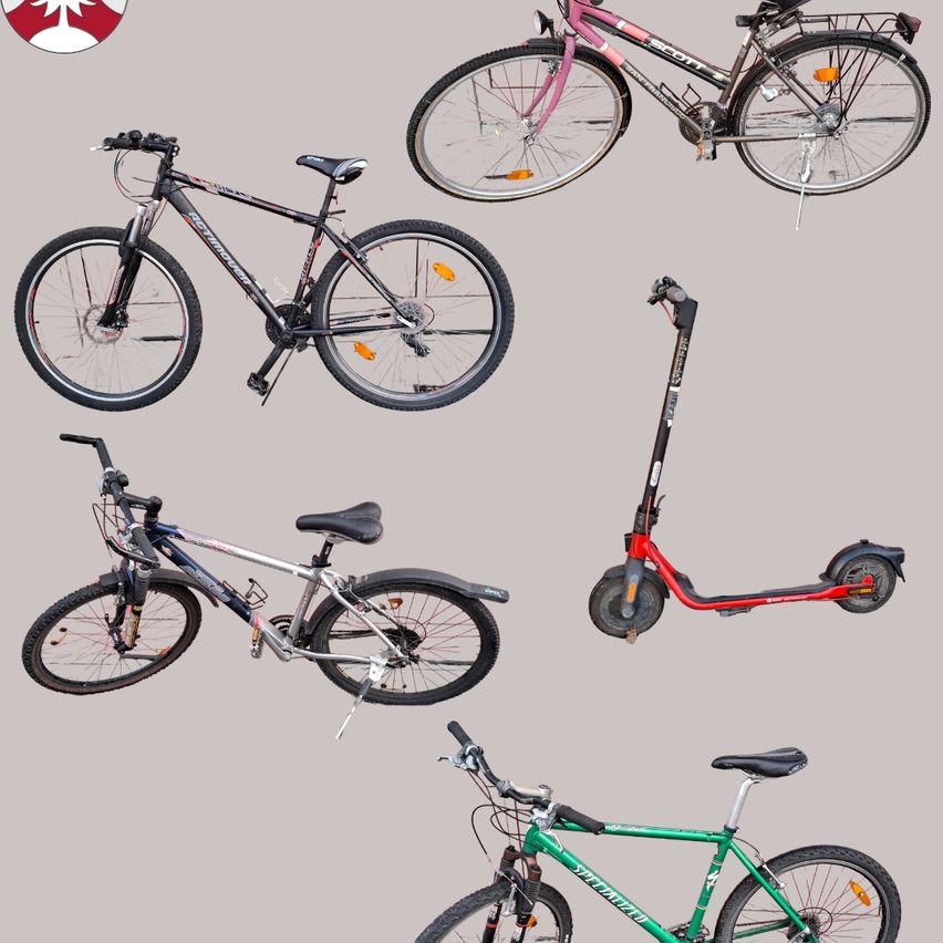 Five different bicycles and a scooter are displayed. There are two black bicycles, one blue, one green, and one pink. The scooter is red.