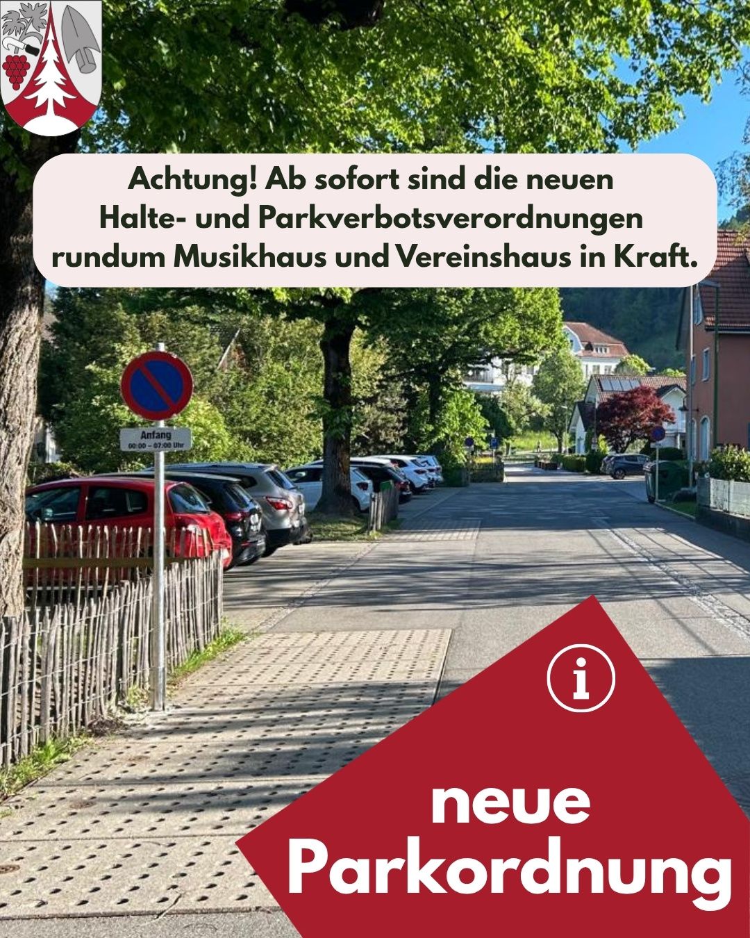 Ein rotes Auto und mehrere andere Autos sind am Straßenrand geparkt. Ein Informationsschild ist am Bürgersteig angebracht. Bäume und Häuser sind im Hintergrund zu sehen.