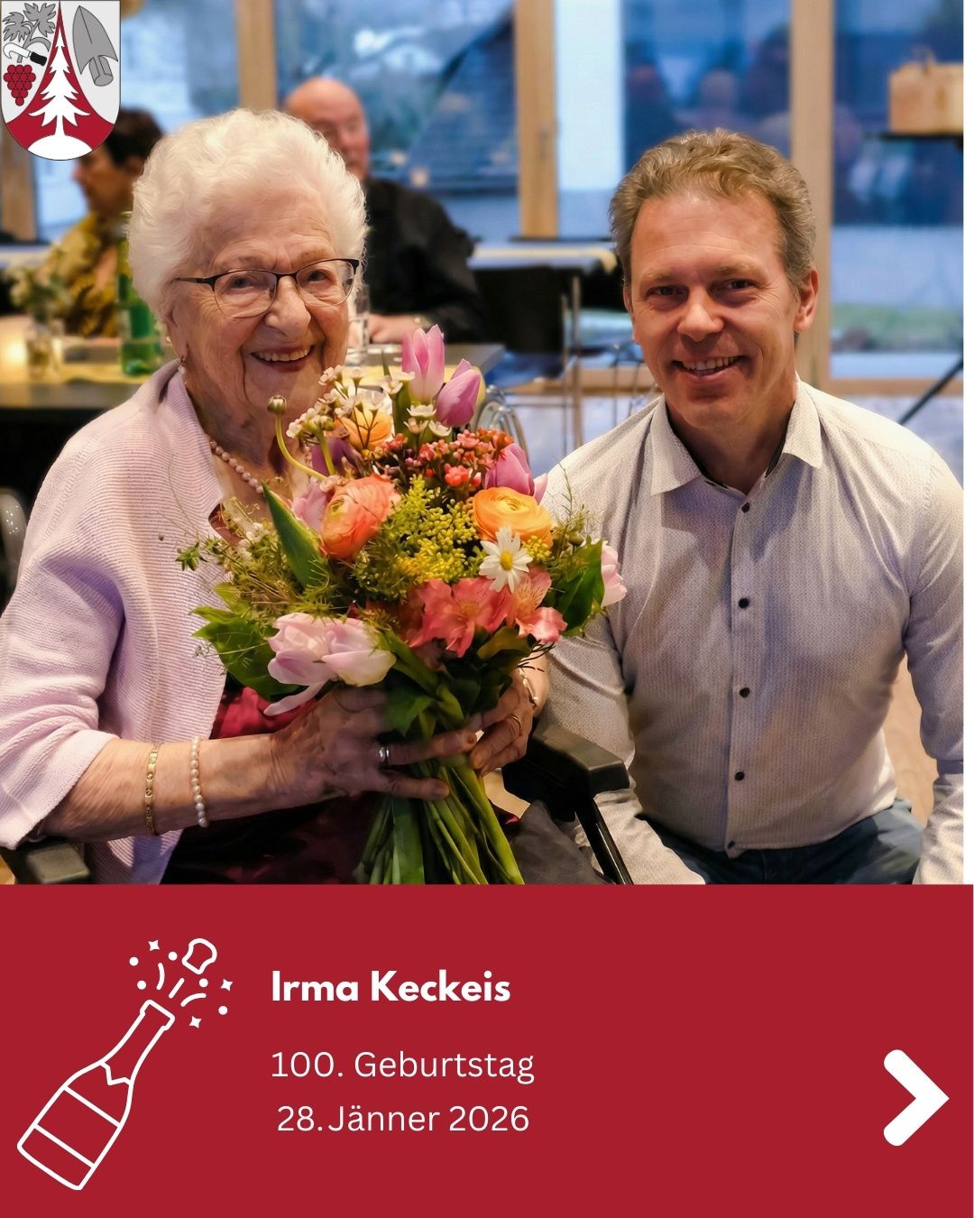 A smiling elderly woman in glasses holds a bouquet of flowers while sitting next to a smiling man. A birthday banner for Irma Keckeis' 100th birthday is displayed below.