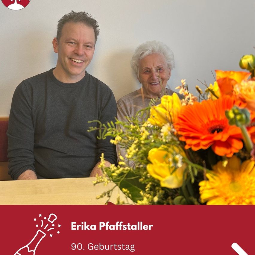 Ein Mann und eine ältere Frau lächeln und sitzen nebeneinander, um ein Foto mit einem Blumenstrauß vor ihnen zu machen. Die Frau feiert ihren 90. Geburtstag.