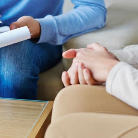 Ein Mann und eine Frau sitzen zusammen und halten Händchen, wobei der Mann einen Stift und Papier in der Hand hat.