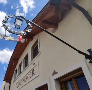 Ein Gebäude mit einem Schild, das Hartberger liest, einer Lampe und einem Kranz, der unter einem blauen Himmel vom Dach hängt.